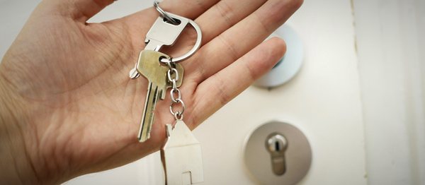 A pair of house keys with a small house keyring resting in an open hand at a front door